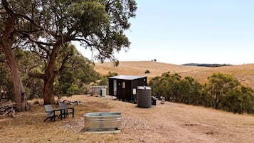 A rustic cabin with a water tank and a bench in a dry, hilly landscape.