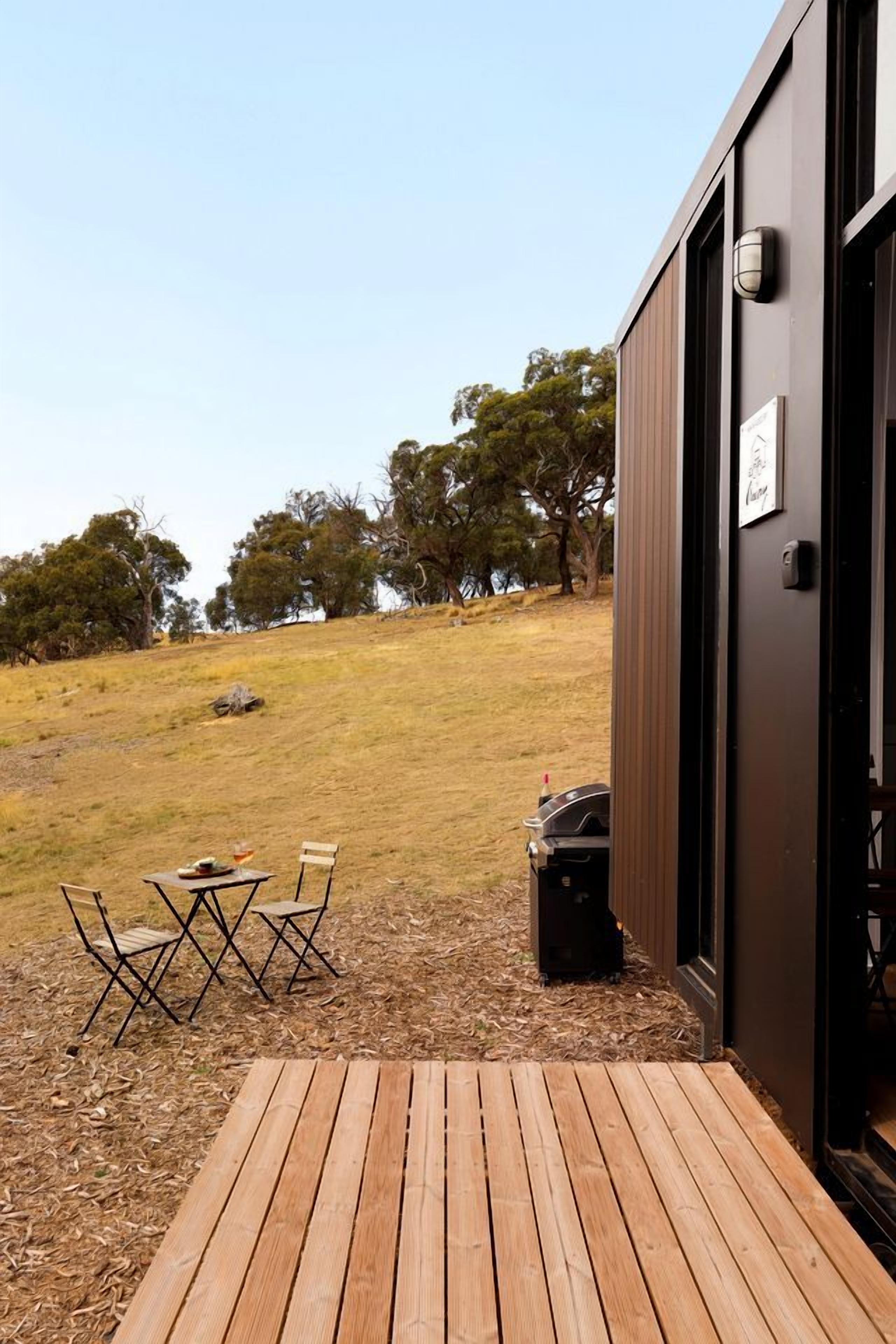 Une terrasse en bois menant à un bâtiment équipé d’un barbecue et d’un espace salon extérieur.