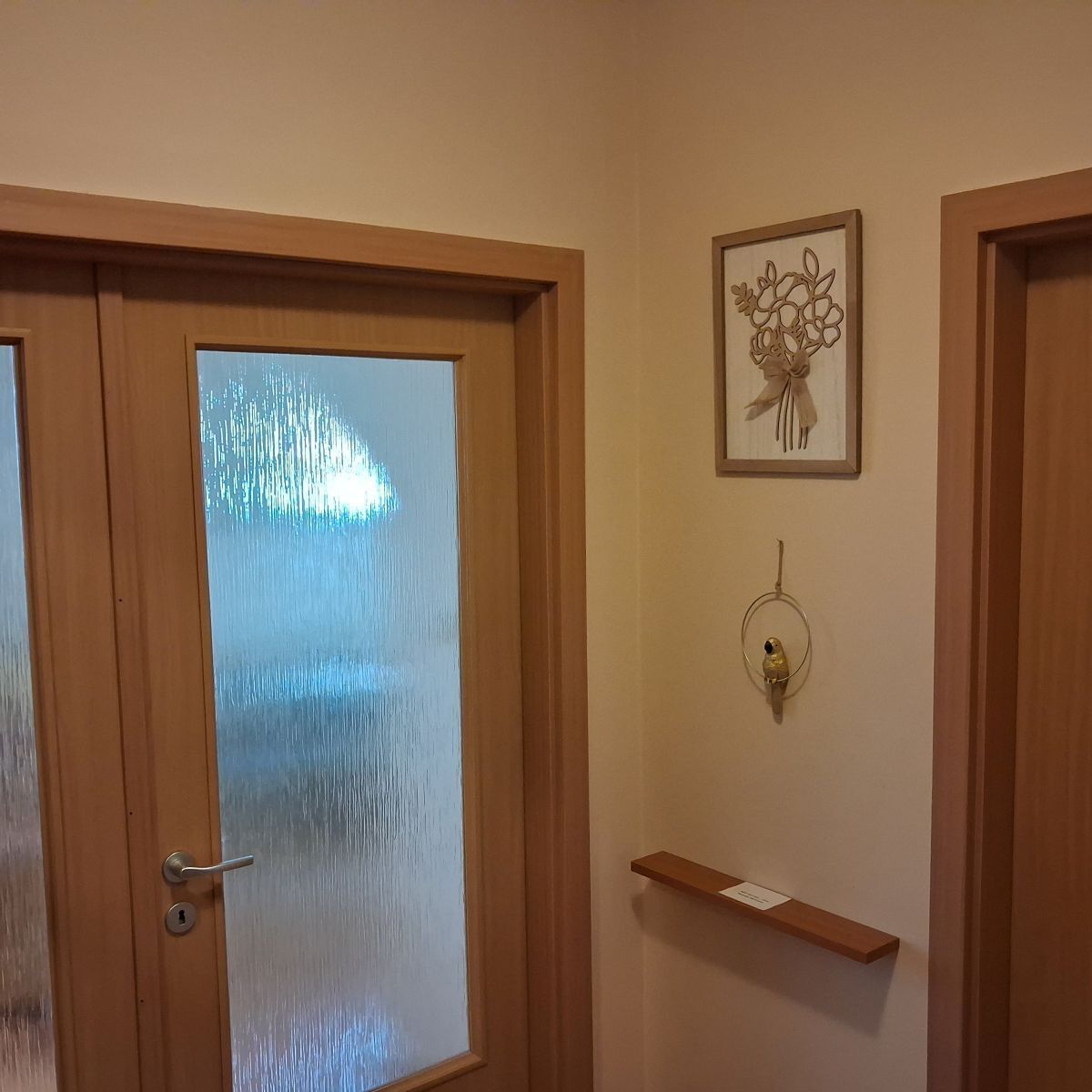 Uma porta de madeira com painel de vidro jateado, um objeto decorativo fixado na parede e uma pequena prateleira de madeira.