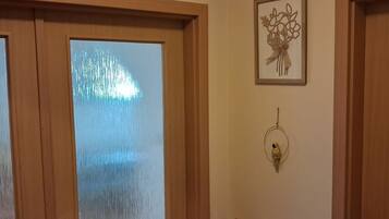 Uma porta de madeira com painel de vidro jateado, um objeto decorativo fixado na parede e uma pequena prateleira de madeira.