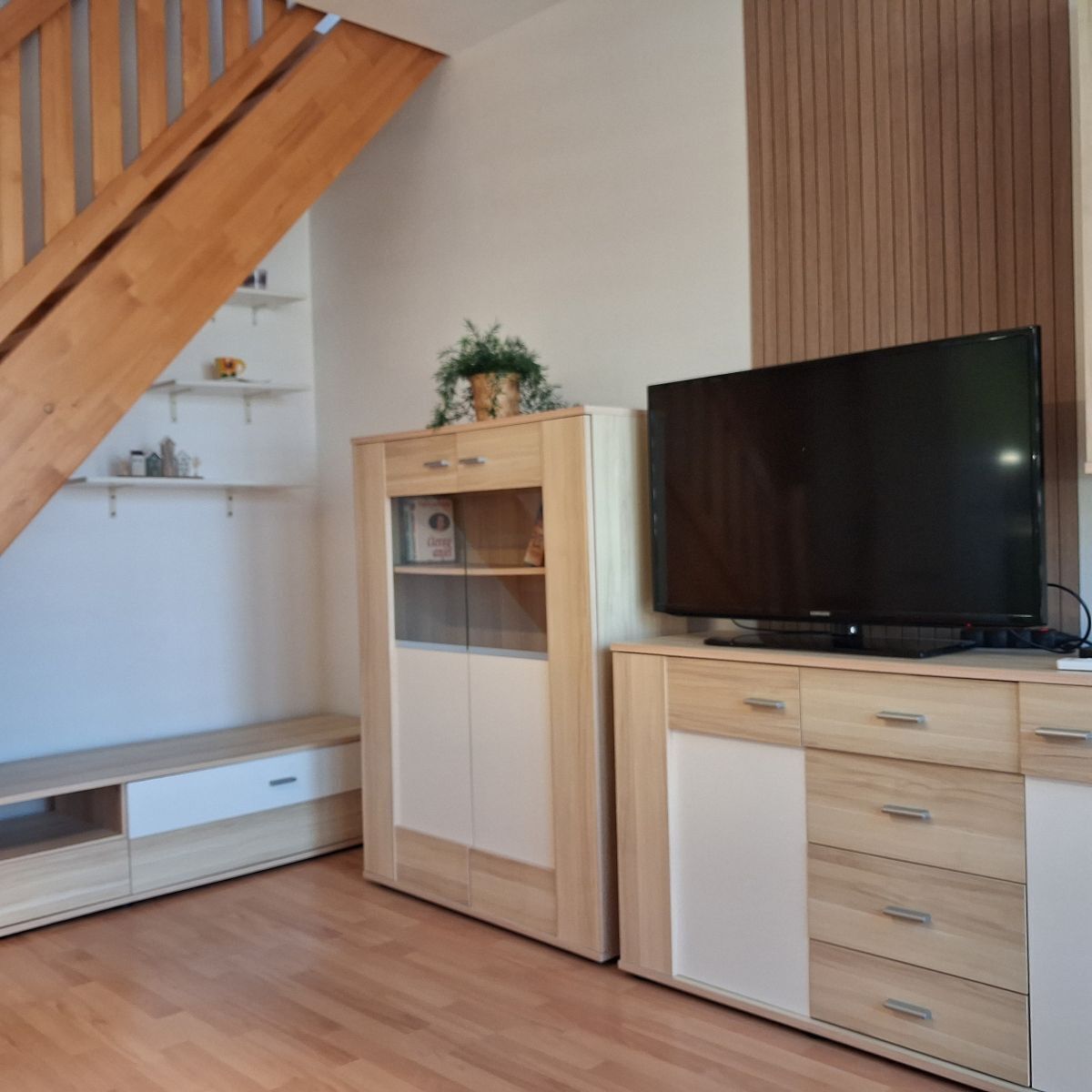 Un soggiorno moderno con una scala in legno, scaffali a muro, una televisione a schermo piatto e un armadio in legno.