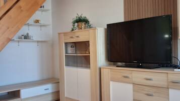 Un soggiorno moderno con una scala in legno, scaffali a muro, una televisione a schermo piatto e un armadio in legno.