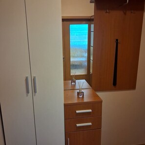 A room with a wooden wardrobe, a small table with a window, and a door with a black handle.