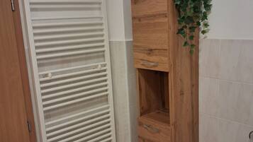Ein Badezimmer mit weißem Heizkörper, einem Holzschrank mit Pflanze darauf und einer Tür.
