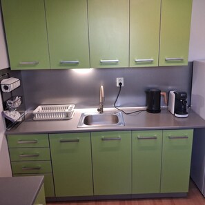A kitchen with green cabinets, a stainless steel sink, a kettle, and a coffee maker.