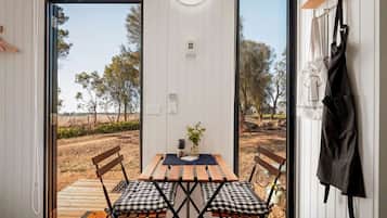 Una habitación con una mesa y sillas de madera, un banco y vista a un espacio exterior con árboles y un sendero de tierra.