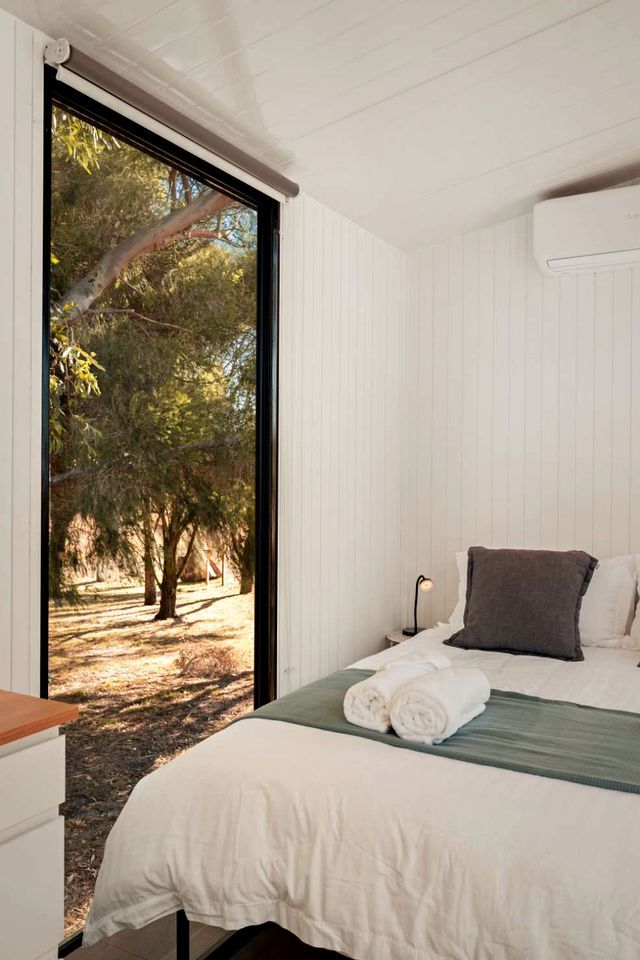 Une chambre à coucher avec un lit, une table de chevet, une lampe et une fenêtre donnant sur des arbres.