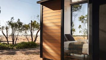 A modern bedroom with a large sliding glass door, a bed with pillows, and a view of the surrounding landscape.