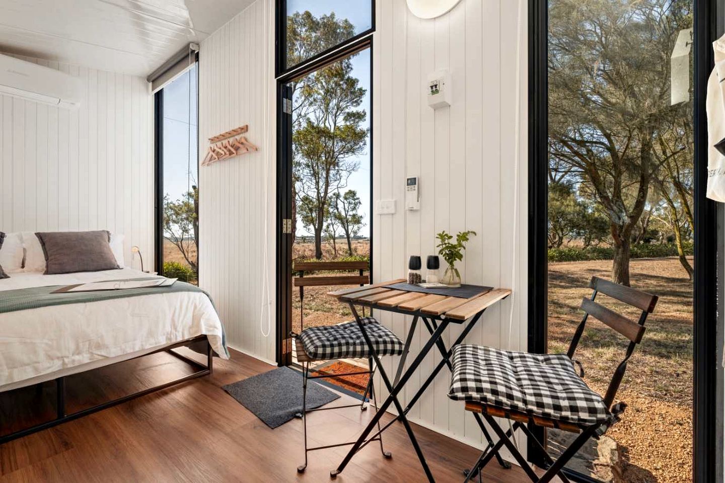 Un dormitorio con cama, escritorio y silla, una ventana y vista a árboles.