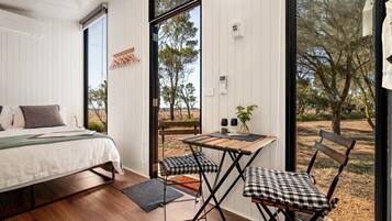 Un dormitorio con cama, escritorio y silla, una ventana y vista a árboles.