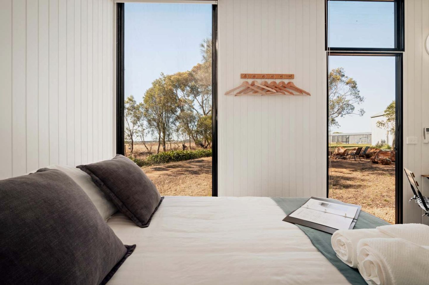 Un dormitorio con cama, almohadas, un perchero de madera y vista al exterior.