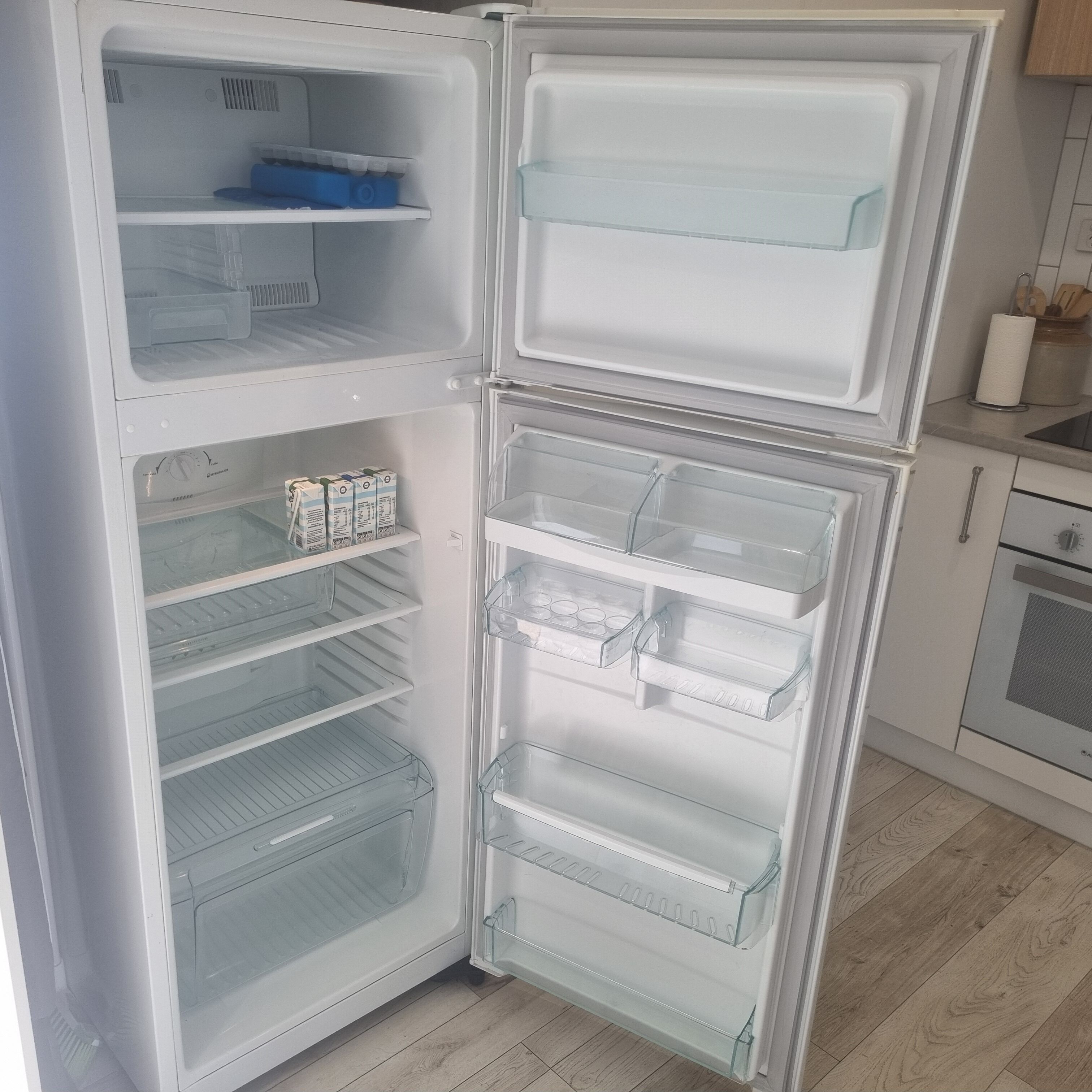 A white refrigerator with multiple shelves and drawers, a blue container on the top shelf, and a paper towel holder on the right side.