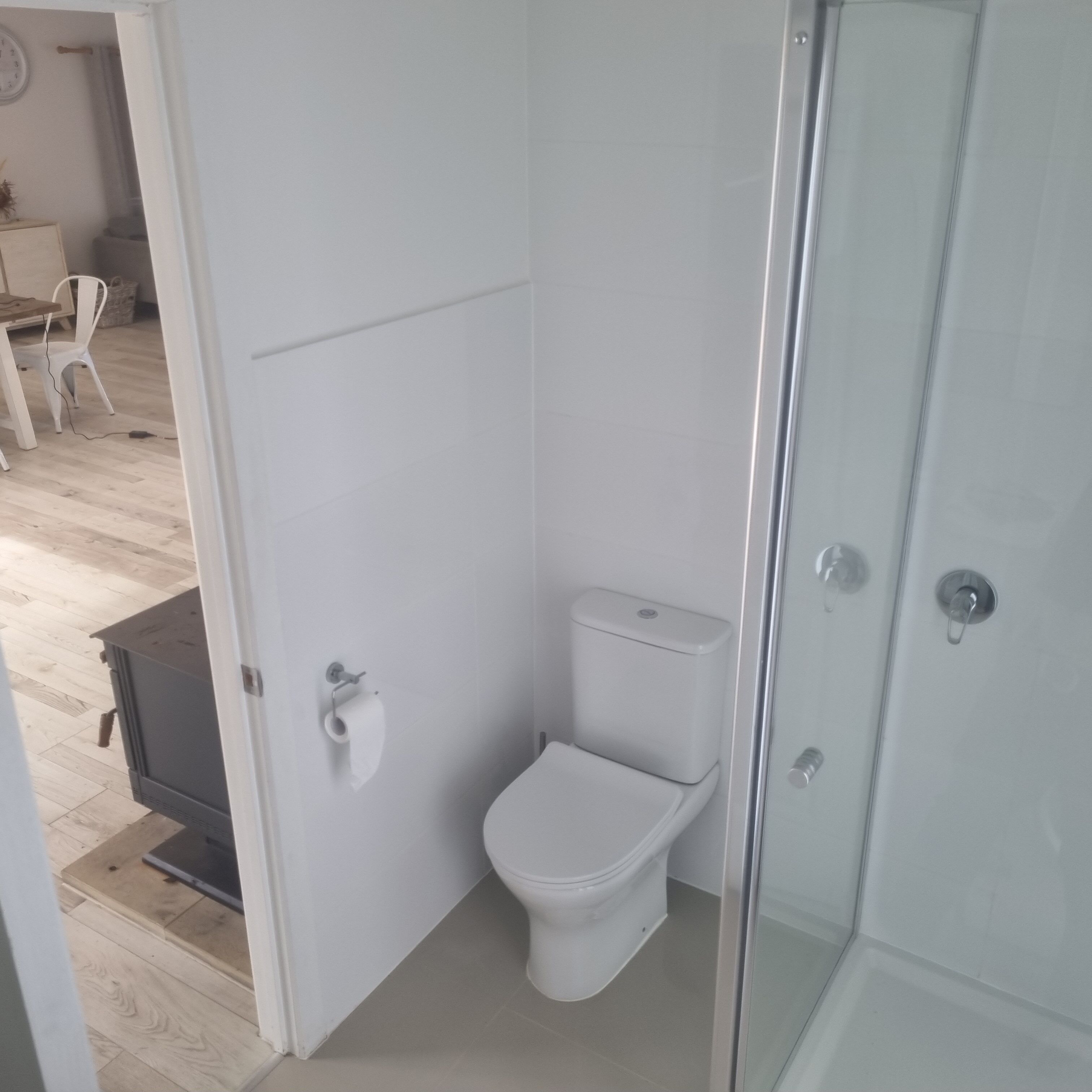 Un baño con inodoro, cabina de ducha y puerta que da a un comedor.