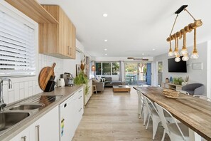 A modern kitchen with a wooden countertop, stainless steel sink, and a dining area with a wooden table and chairs. - Prosser River Retreat - Gateway to Maria Island (Orford)