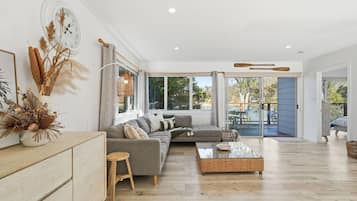 A spacious living room with a grey sectional sofa, a coffee table, and a large window providing a view of the outdoors.