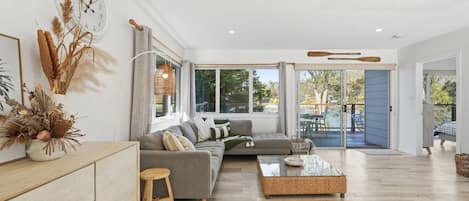 A spacious living room with a grey sectional sofa, a coffee table, and a large window providing a view of the outdoors.