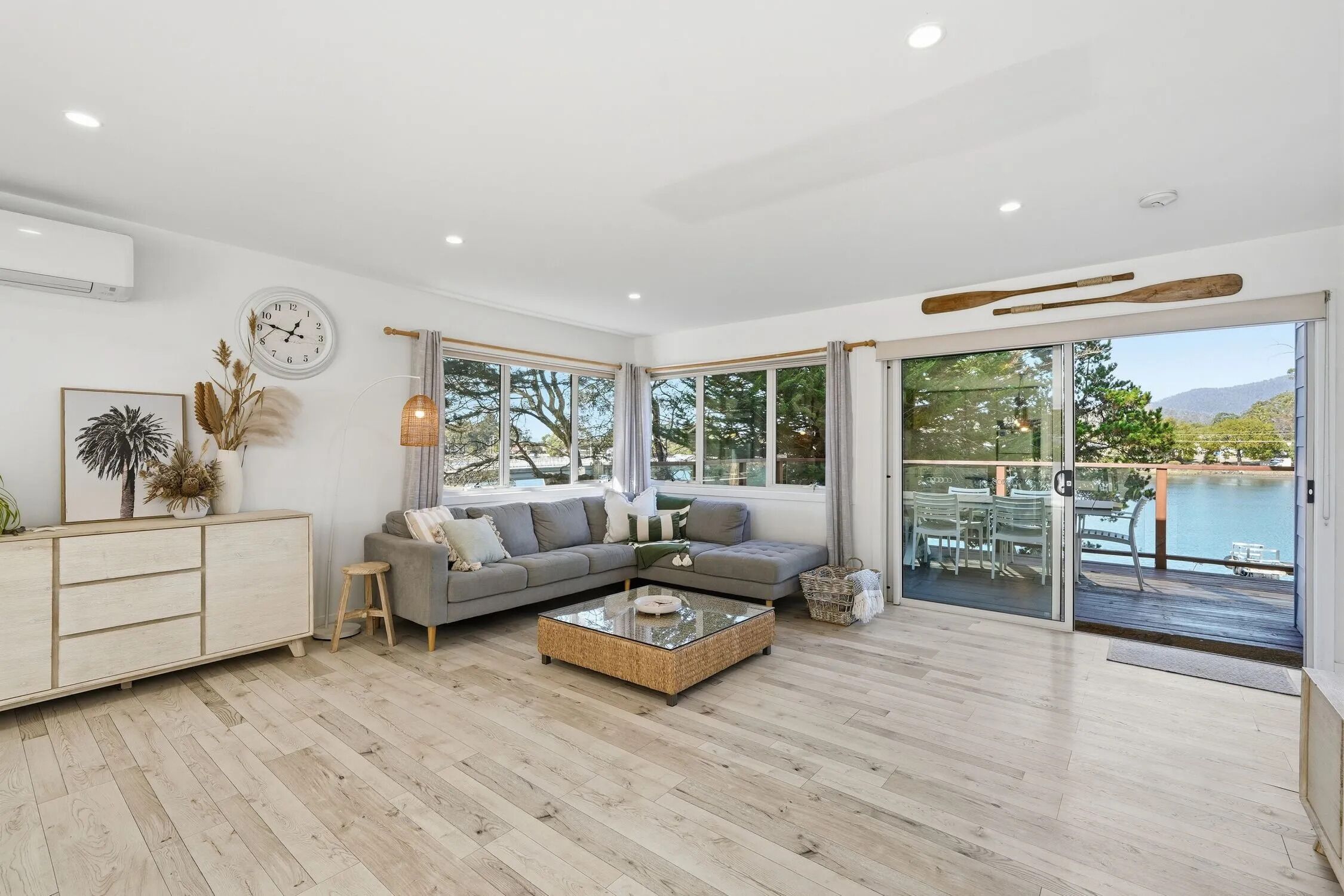 A modern living room with a grey sectional sofa, a glass coffee table, and a view of a pool through large windows.