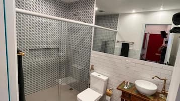 A modern bathroom with a glass-enclosed shower, a white toilet, a wooden vanity with a sink, and a mirror above the vanity.