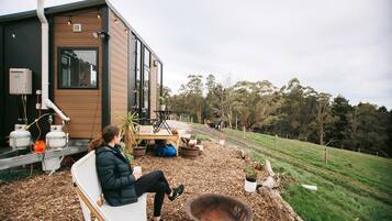 A modern house with a large window, outdoor seating, and a fire pit.