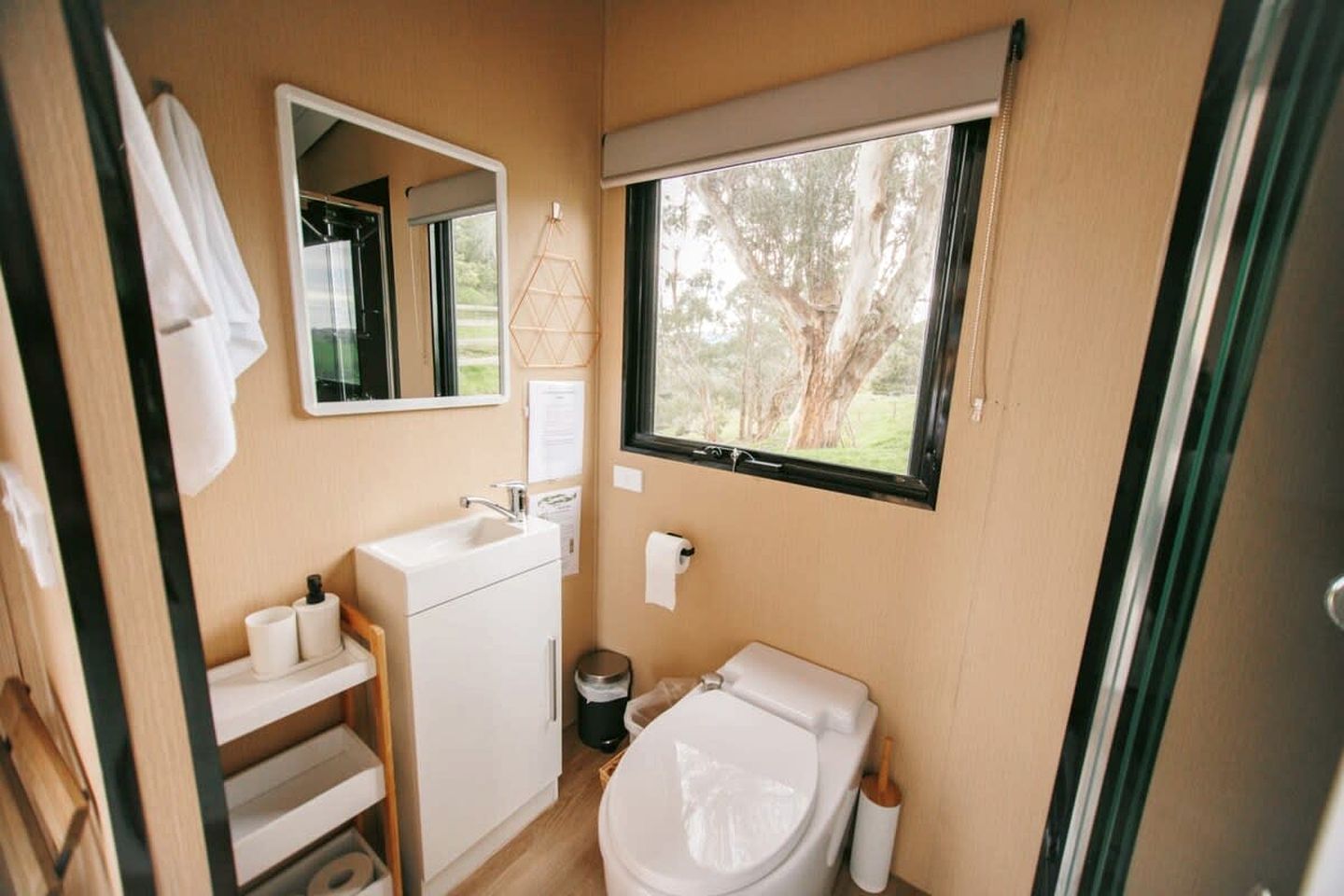 A compact bathroom with a sink, toilet, and a window providing a view of trees.