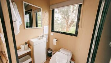 A compact bathroom with a sink, toilet, and a window providing a view of trees.