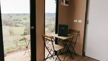 A room with a view of a rural landscape, a wooden table with a black folder, and a bench.