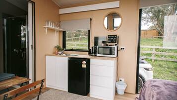Une petite cuisine équipée d’un four à micro-ondes, d’un petit évier et d’une machine à café. Un panneau d’accueil est placé au-dessus du four à micro-ondes, et une fenêtre offre une vue sur l’extérieur.