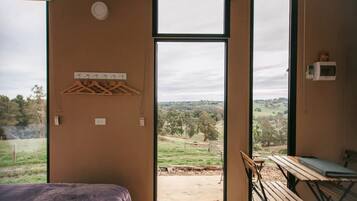 A room with a bed, a table, and a view of a rural landscape through a large window.