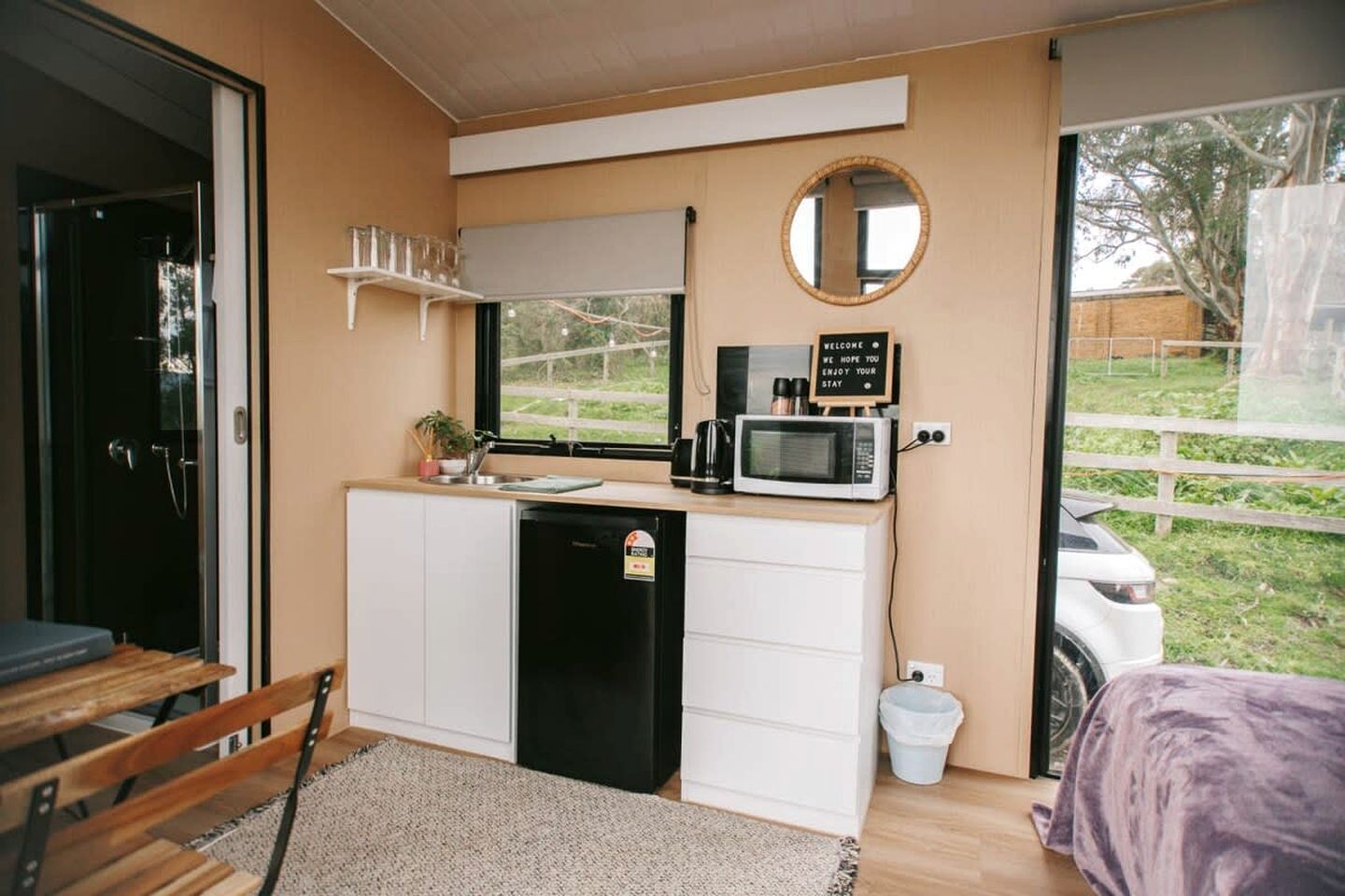 A compact kitchenette with a microwave, a small sink, and a coffee maker. There is a welcome sign above the microwave, and a window with a view of the outdoors.