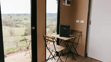 A room with a view of a rural landscape, a wooden table with a black folder, and a bench.