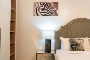Ein Hotelzimmer mit einem Bett, einem Nachttisch mit Lampe, einem Zebrabild an der Wand und einem Holzschrank.