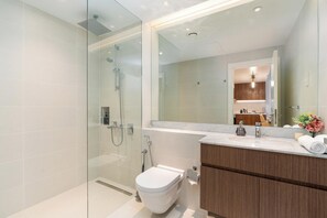 A modern bathroom with a glass shower enclosure, a toilet, a vanity with a mirror, and a sink. - bnbme - La Cote 3 - 1BR (Dubai)