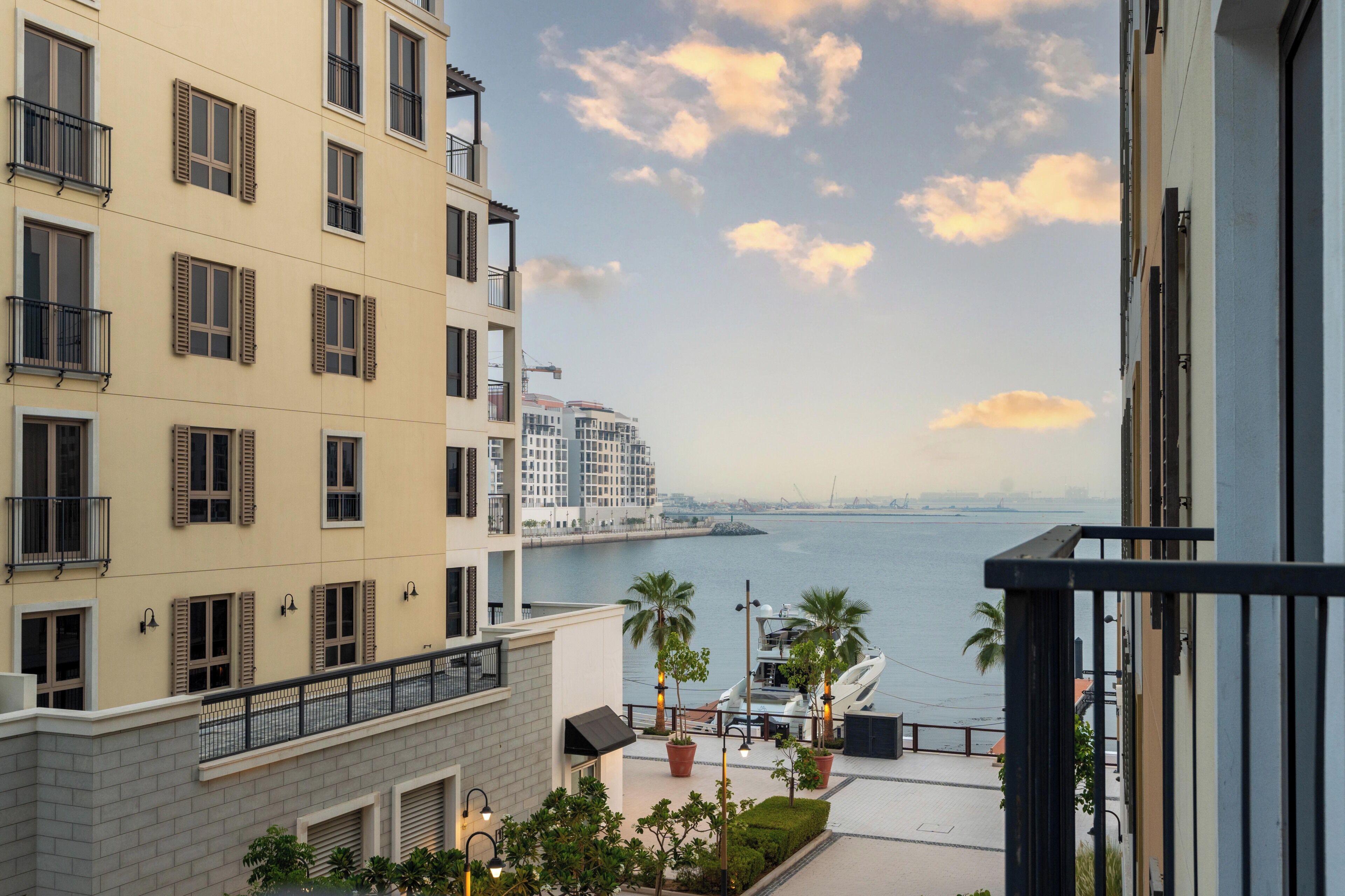 Un immeuble de grande hauteur doté de nombreux balcons et offrant une vue sur une étendue d’eau, avec une silhouette urbaine visible au loin.