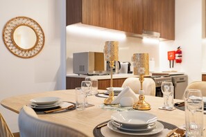 A dining table set with plates, glasses, and cutlery, with a decorative lamp and a mirror on the wall. - bnbme - La Cote 3 - 1BR (Dubai)