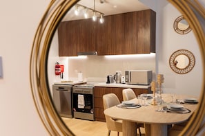 A modern kitchen with wooden cabinets, stainless steel appliances, and a dining area with a round table set for four. - bnbme - La Cote 3 - 1BR (Dubai)