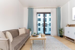 A modern living room with a sofa, a coffee table, and a view of a building through a glass door. - bnbme - La Cote 3 - 1BR (Dubai)