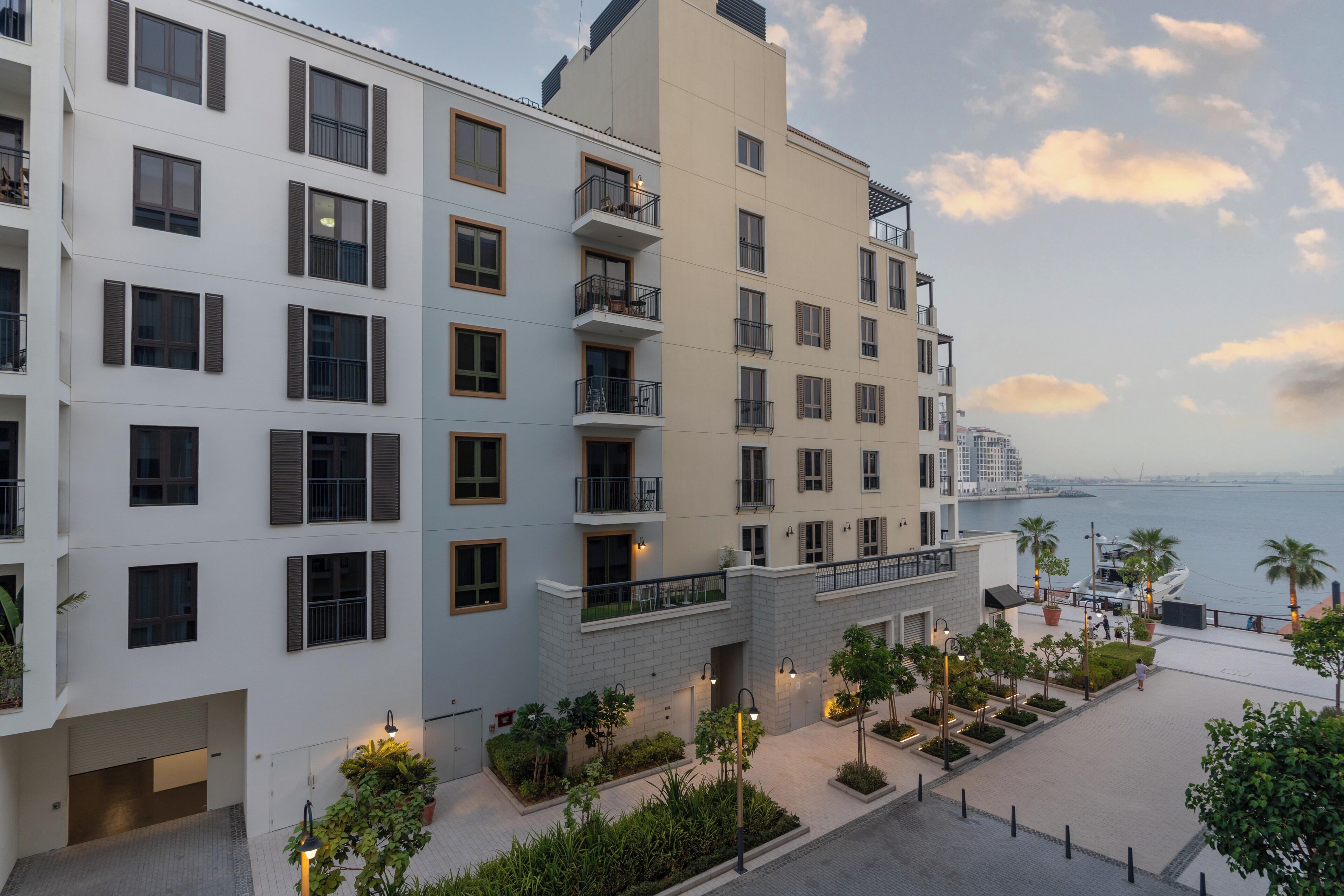 Un hôtel à plusieurs étages doté de balcons, offrant une vue sur le front de mer et comprenant une cour aménagée.