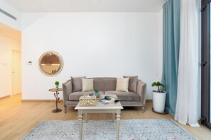 Una sala de estar con un sofá, una mesa de centro, una mesita auxiliar, una planta en maceta y un espejo en la pared.