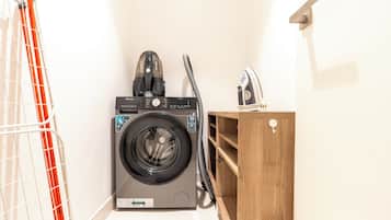 A compact laundry area with a front-loading washing machine, a steam iron, and a drying rack.