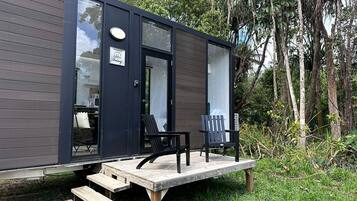A modern cabin with a deck, two chairs, and a small table.