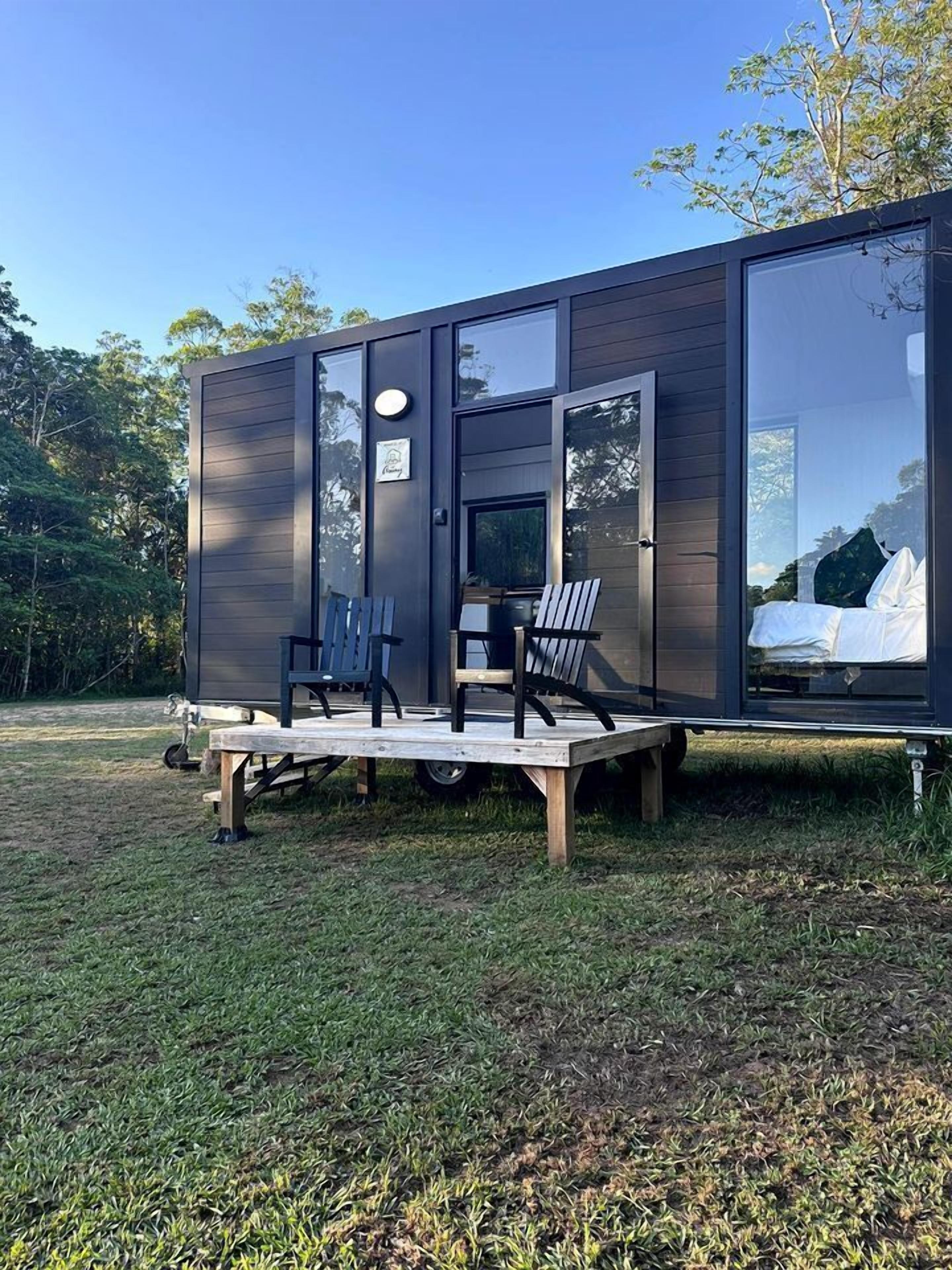 A modern, compact cabin with a deck, seating area, and a visible bed inside.