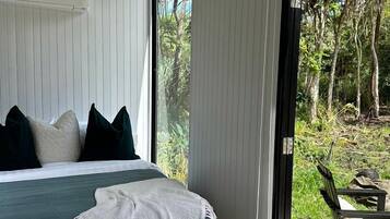 A bedroom with a bed, pillows, a blanket, and a view of the outdoors through a glass door.