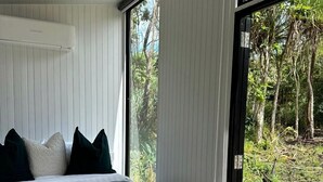 A bedroom with a bed, pillows, a blanket, and a view of the outdoors through a glass door.