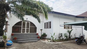 A white building with a large arched entrance, steps leading up to the door, and a motorcycle parked in front. - Premium Single Room Ne A&C Mall W/ Premium Amenity (Accra)