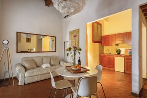 A modern living room with a sofa, dining table, and chairs, a kitchen with wooden cabinets, and a large mirror on the wall. - Via Maggio 10 – Historic 1 Bedroom in Oltrarno (Florence)