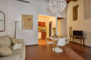 Ein Wohnzimmer mit Sofa, einem Esstisch mit Stühlen, einem Bild an der Wand und einer Küche im Hintergrund.