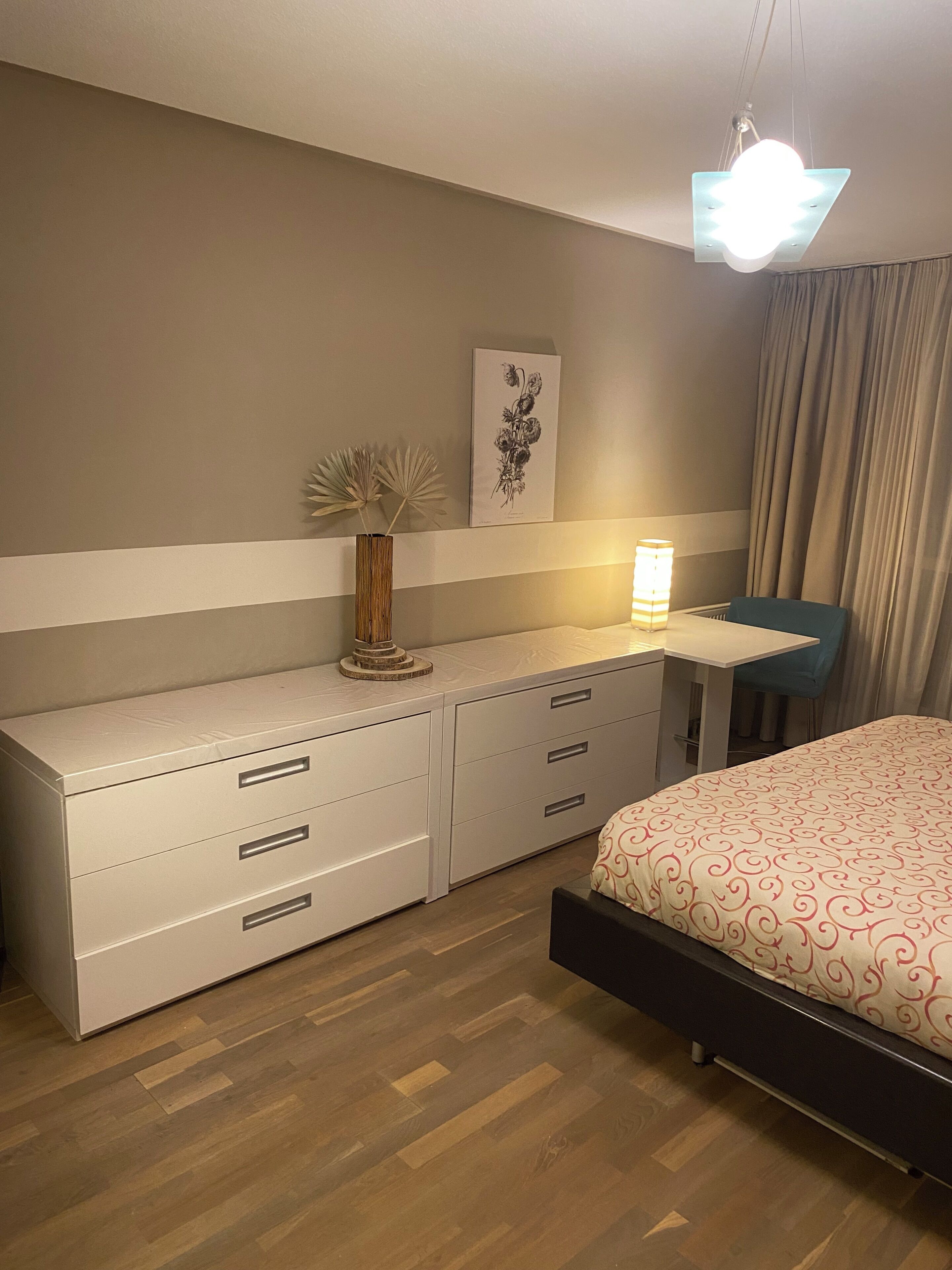 Une chambre à coucher comprenant un lit, une table de chevet, une lampe, une commode et un tableau accroché au mur.