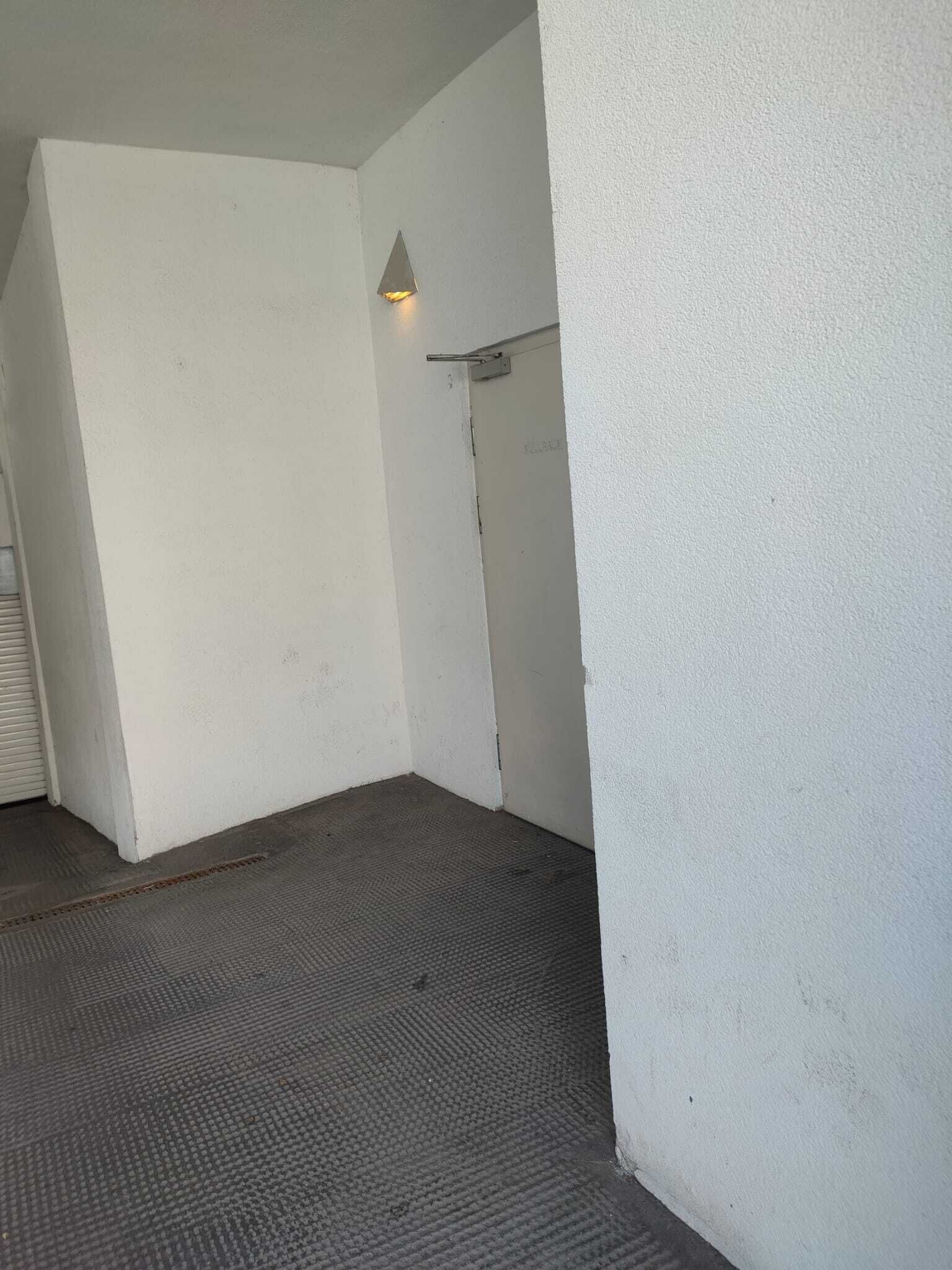 Huoneen nurkka, jossa on kuvioitu lattia, valkoiset seinät ja pieni valaisin.