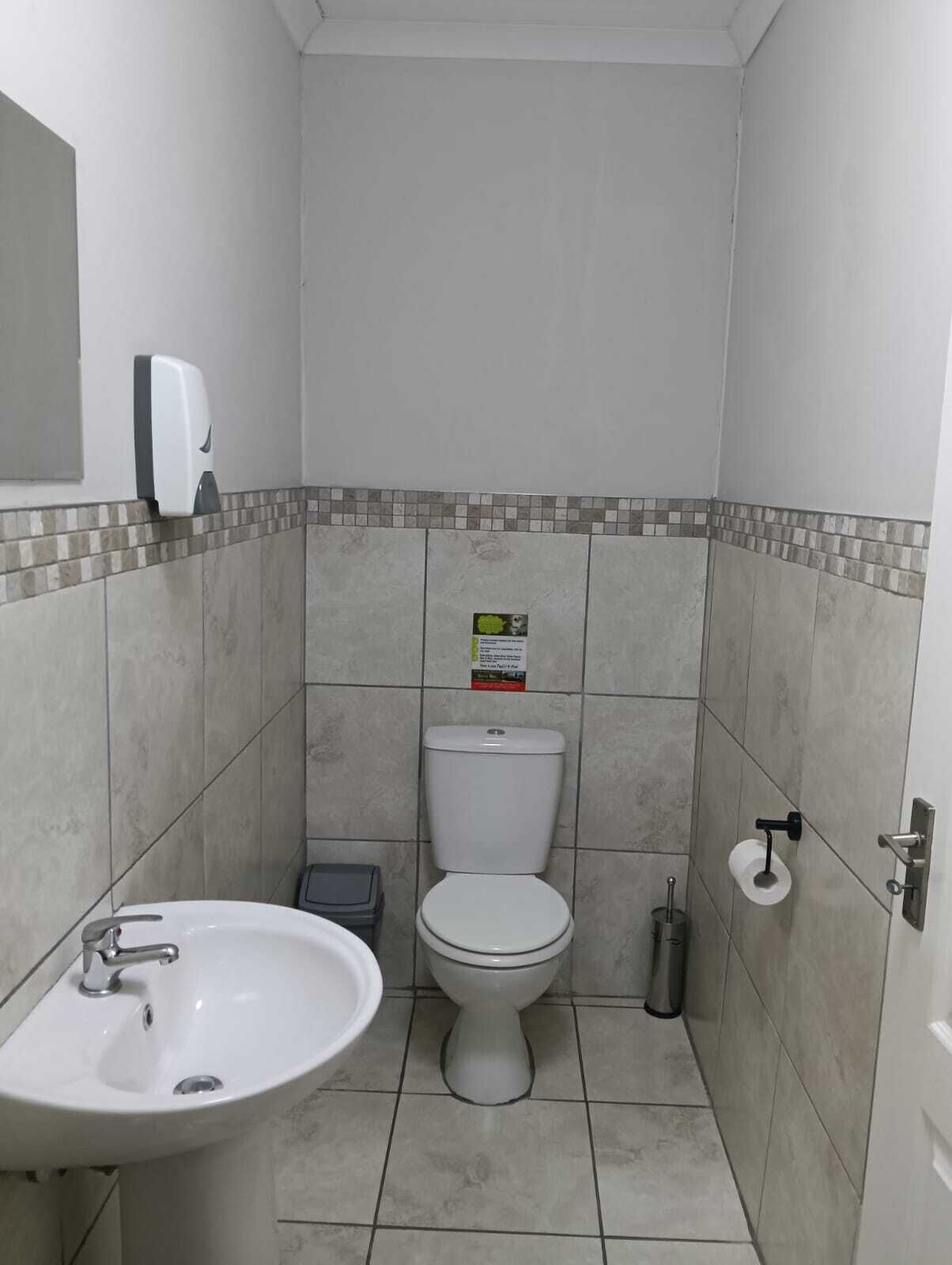 Une petite salle de bain propre, avec un lavabo, des toilettes et un sèche-mains, le tout de couleur blanche.