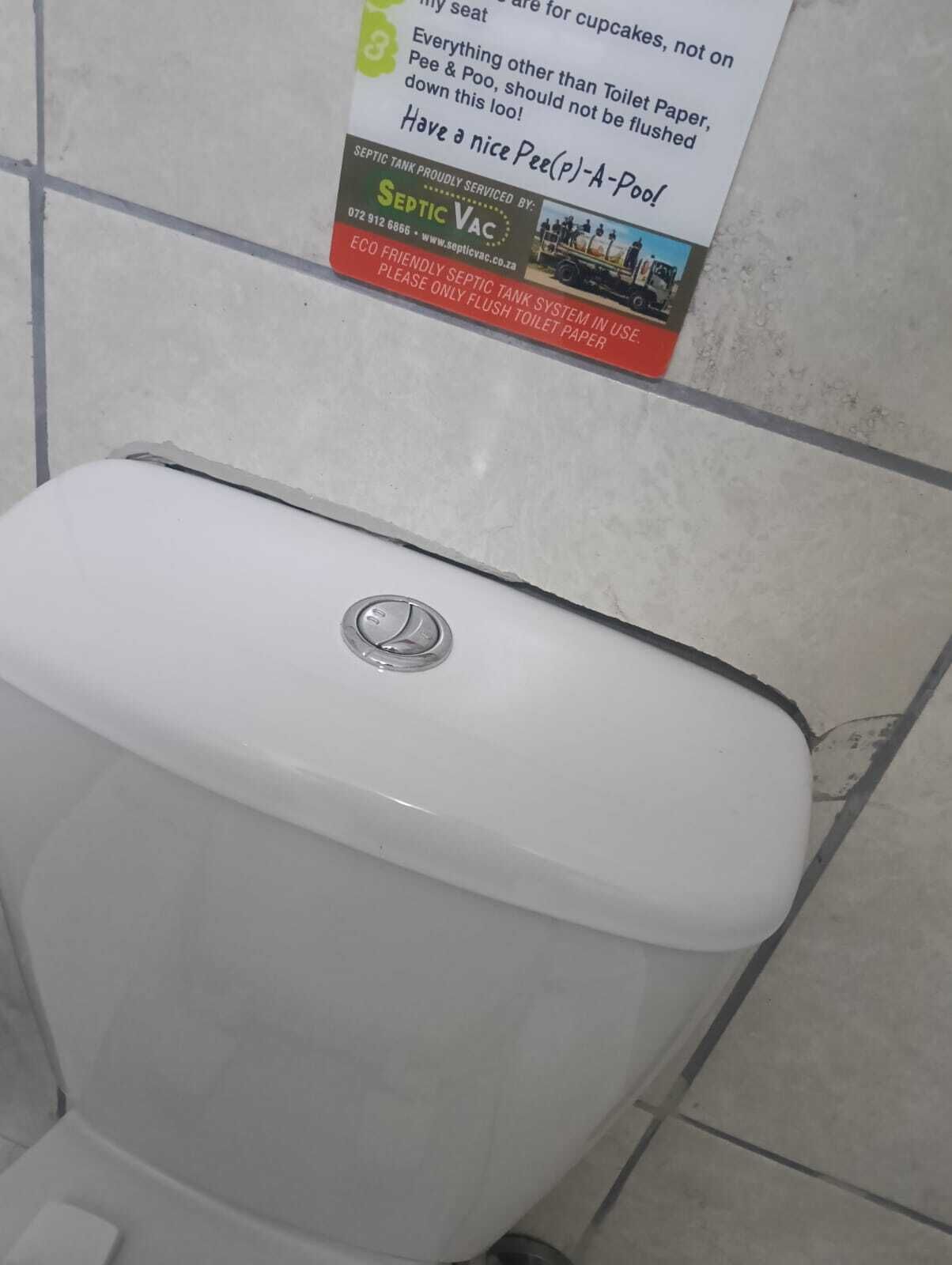 Des toilettes avec un autocollant indiquant la présence d’une fosse septique, apposé sur le mur au-dessus.